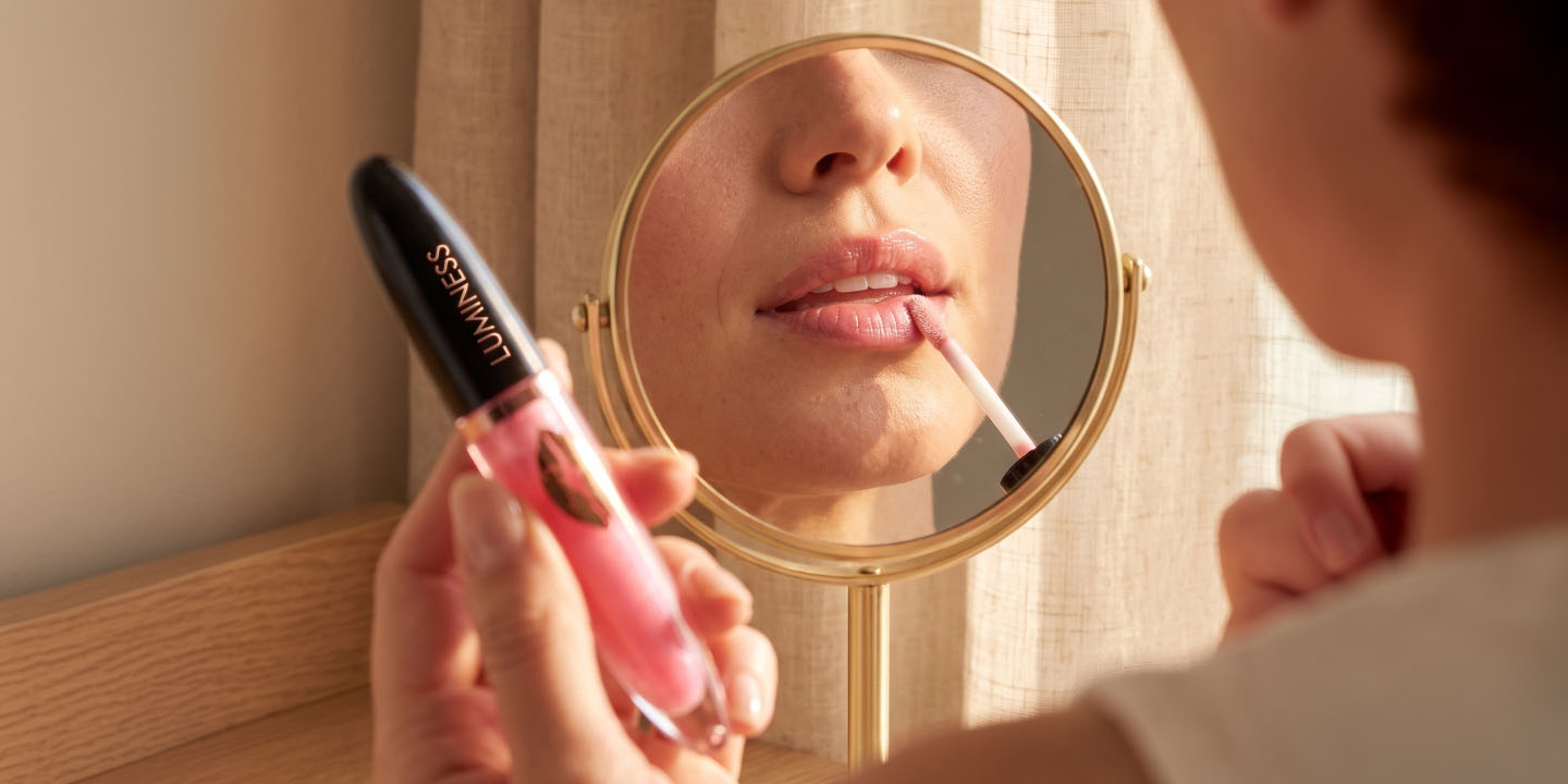 Luminess gentle lip booster being applied while checking the lip finish in a mirror